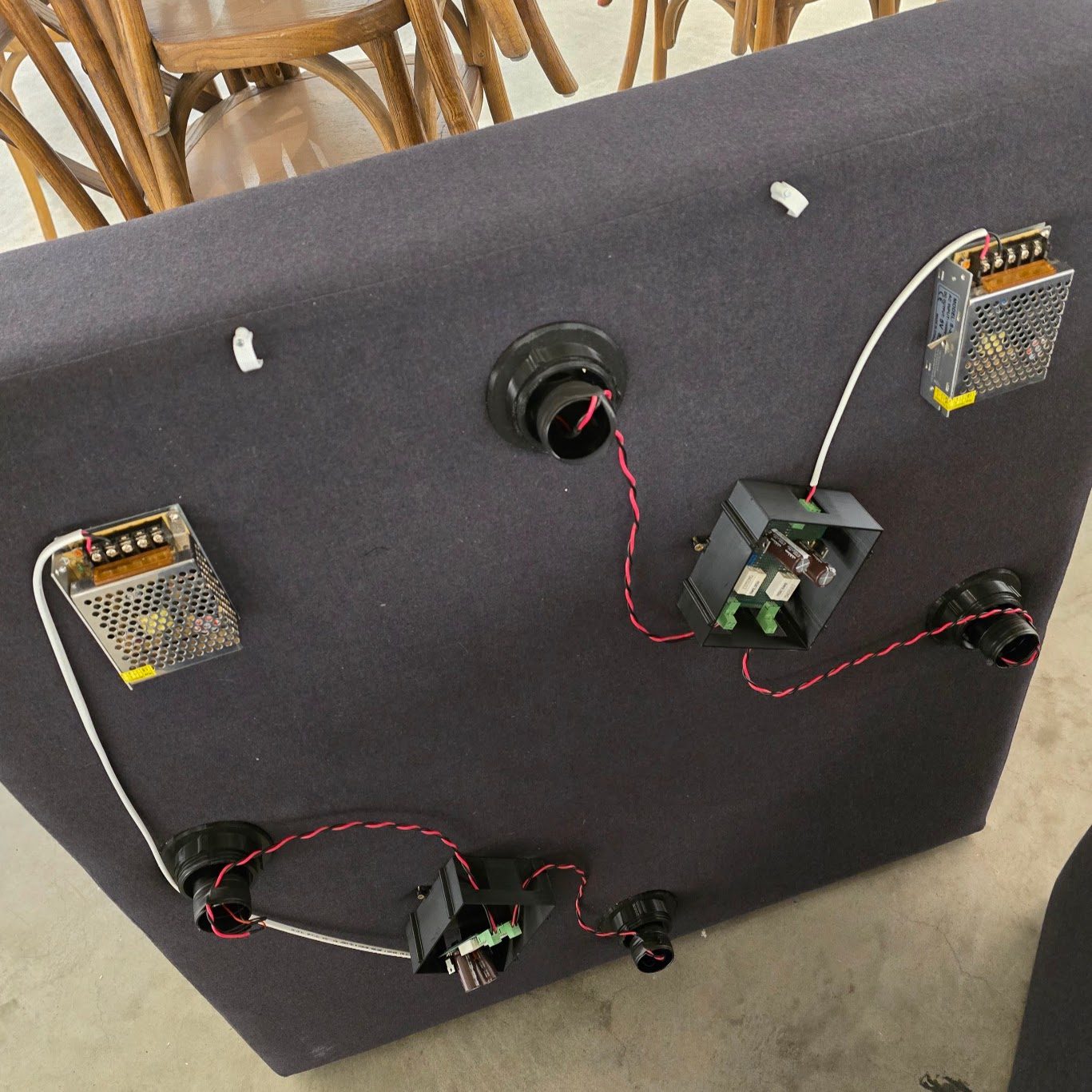 The box top seen from above, upside down, with two metal 5 V supplies, two printed driver-board enclosures and the four light-mount bodies passing through the panel, wired in twisted red-black pairs