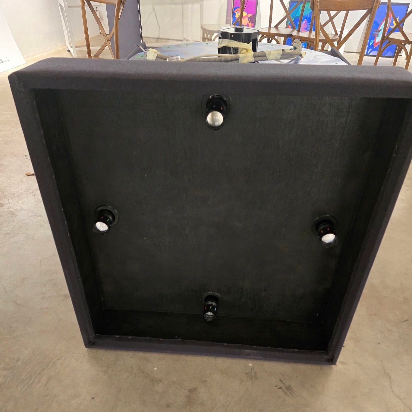 The underside of the box top, lined in black, with four torch-head LEDs on ball mounts set one at the midpoint of each edge, all aimed down into the box