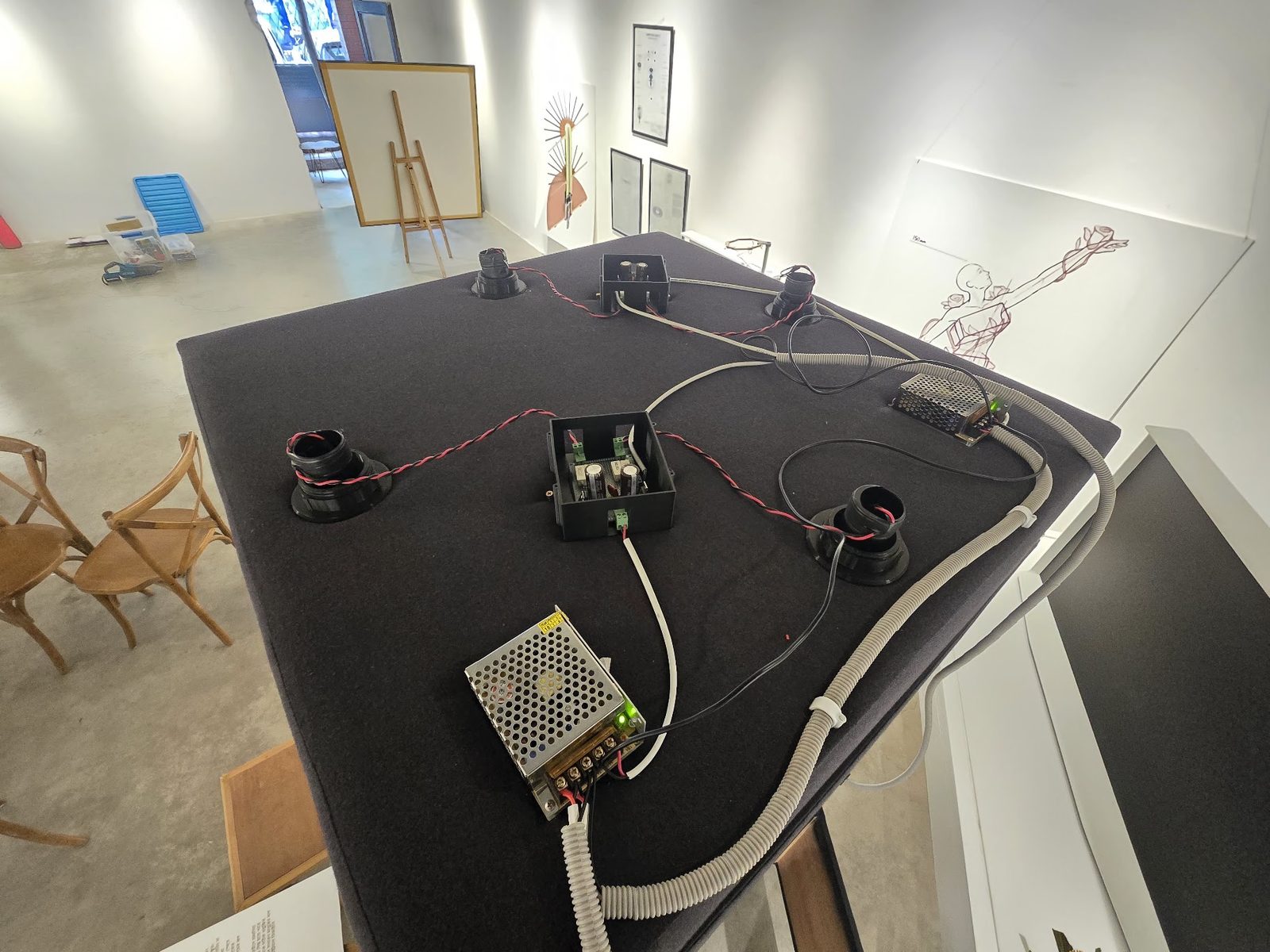 The box top resting upside down in the gallery during install, wired up — two supplies, two driver boards, the four light mounts and flexible conduit running off the edge